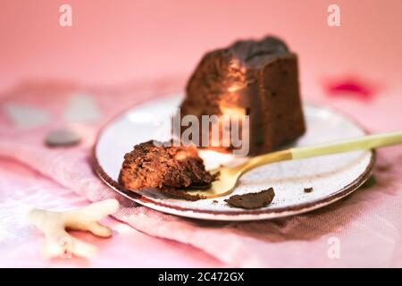 Une tranche d'un gâteau au chocolat avec des pommes sur une assiette blanche, un morceau de gâteau sur une fourchette d'or près. Serviette et arrière-plan roses. Des taches de lumière sur le Banque D'Images