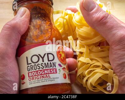 Gros plan sur les mains d'un homme tenant un pot de sauce bolognaise de marque Loyd Grossman dans une main, avec quelques tagliatelles non cuites dans l'autre. Banque D'Images