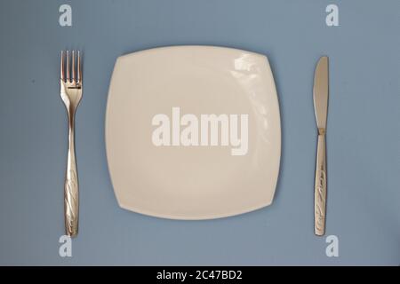 Vider la plaque, la fourchette et le couteau sur fond bleu. Nettoyez l'assiette et les couverts sur un fond clair. Vue de dessus. Pose à plat. Banque D'Images