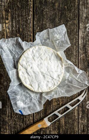 Fromage Brie. Fromage blanc doux avec moule blanc enveloppé de papier sur une ancienne table en bois. Vue de dessus. Banque D'Images