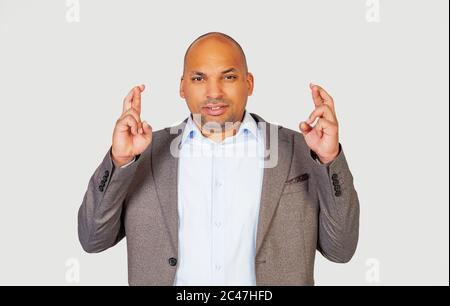 Un jeune homme afro-américain élégant croise les doigts avec une expression inquiète, demandant à Dieu de croiser les doigts avec un regard pitoyable en espérant que le patron n'a pas remarqué qu'il était en retard pour le travail Banque D'Images