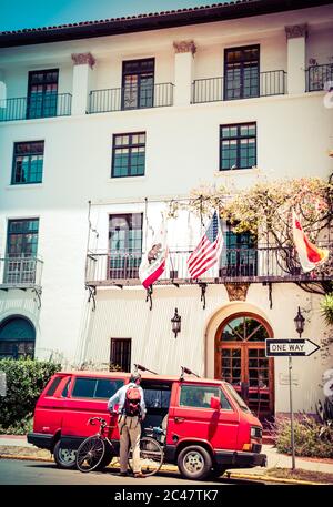 Vue arrière d'un homme plus âgé chargeant un vélo dans Volkswagen Vanagon rouge vintage, en face d'un bel immeuble de style espagnol à Santa Barbara, CA, Etats-Unis Banque D'Images