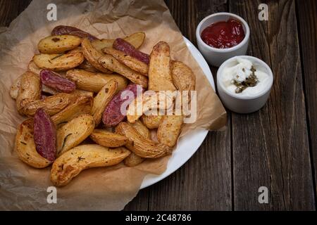 Pommes de terre frites à l'air, en quartiers violets et jaunes, servies avec de la crème et du ketchup sur une table en bois, espace pour les copies Banque D'Images