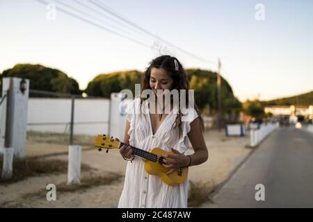 Photo avec mise au point peu profonde d'une femme souriante jouant un jaune ukulele sur le côté d'une route Banque D'Images