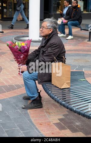 Un homme asiatique âgé pratiquant la distanciation sociale se trouve dans un espace public avec un bouquet de fleurs Banque D'Images