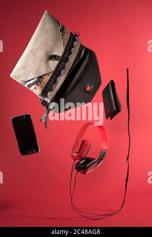 Prise de vue verticale d'un smartphone, d'un casque, d'un portefeuille provenant d'un petit sac isolé sur un fond rouge Banque D'Images