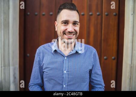 Jeune homme émotionnel avec une chemise bleue debout à la porte avec un petit sourire sur son visage Banque D'Images