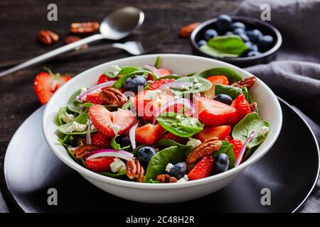 gros plan de la salade d'été de fraises, bleuets, épinards, noix de pacane et feta émietté dans un bol blanc sur une table en bois sombre, paysage Banque D'Images