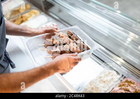 Vendeur mettant plateau avec glace sur un bâton dans le frigo au comptoir d'un magasin, gros plan Banque D'Images
