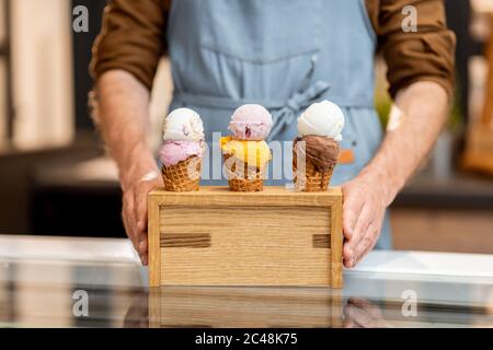 Vendeur mettant un stand avec trois crèmes glacées délicieuses dans des cornets de gaufres avec différentes saveurs sur le comptoir d'un magasin, gros plan Banque D'Images