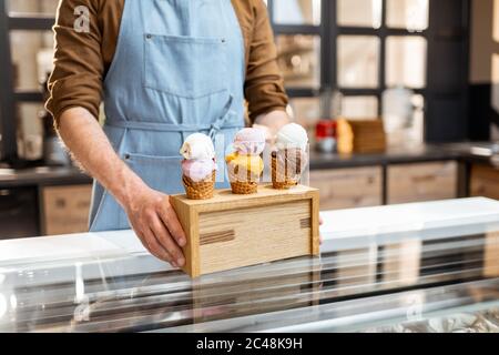 Vendeur mettant un stand avec trois crèmes glacées délicieuses dans des cornets de gaufres avec différentes saveurs sur le comptoir d'un magasin, gros plan Banque D'Images