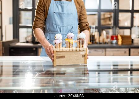 Vendeur mettant un stand avec trois crèmes glacées délicieuses dans des cornets de gaufres avec différentes saveurs sur le comptoir d'un magasin, gros plan Banque D'Images