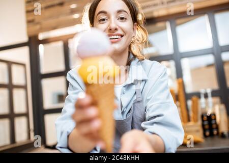 Une femme joyeuse vendait de la glace délicieuse dans un cornet de gaufres à l'intérieur, vendant des bonbons dans la boutique Banque D'Images