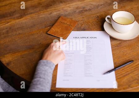 Demande de visa et passeport allongé sur la table au café, main féminine. Banque D'Images