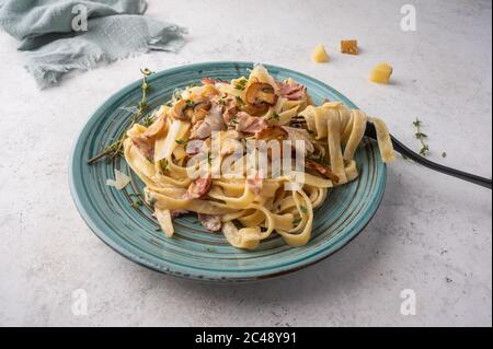 Gros plan sur les pâtes fettuccine avec champignons, bacon, parmesan dans une assiette blanche avec fourchette et serviette sur fond de bois clair Banque D'Images