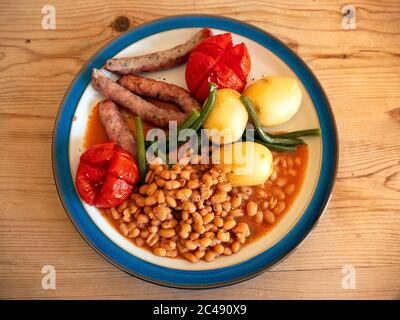Déjeuner plat principal saucisses avec haricots verts pommes de terre nouvelles, haricots italiens tomates grillées et sauce plaque blanche bord bleu de table en bois Banque D'Images