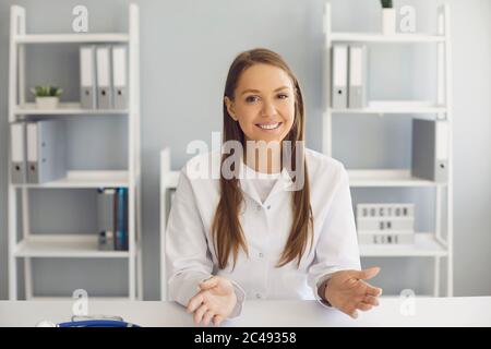 Médecin souriant regardant la caméra, consultant le patient en ligne à la clinique. GP ayant une vidéo conférence avec webcam avec le client Banque D'Images