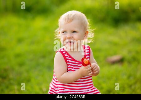 Jolie petite fille souriant dans rouge robe d'été marchant sur la pelouse verte Banque D'Images