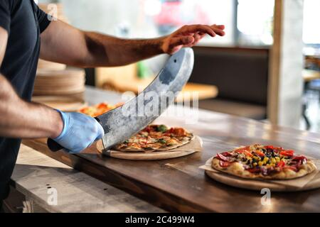 Cuisine, cuisine italienne et concept de cuisine - cuisinez avec une pizza à couper le couteau aux pièces à la pizzeria.Cook's fait la main de pizza maison sur la table. Banque D'Images