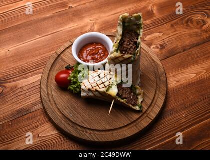 Burrito ou tortilla servi dans le restaurant ou le café. Viande hachée enveloppée de pain de lave-glace sur fond de bois. Pain plat avec garniture de porc ou de poulet et sauce au piment rouge. Concept du plat principal. Banque D'Images