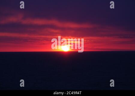 Séquence d'images d'un coucher de soleil, coucher de soleil rouge vif sur mer sombre avec nuages sombres Banque D'Images