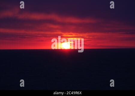 Séquence d'images d'un coucher de soleil, coucher de soleil rouge vif sur mer sombre avec nuages sombres Banque D'Images