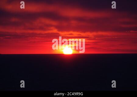 Séquence d'images d'un coucher de soleil, coucher de soleil rouge vif sur mer sombre avec nuages sombres Banque D'Images