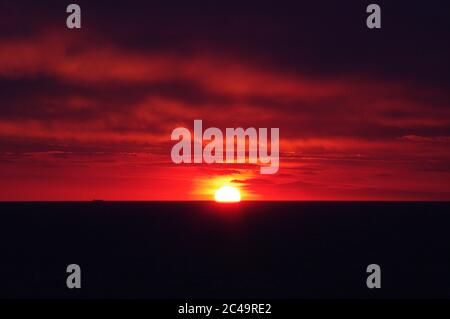 Séquence d'images d'un coucher de soleil, coucher de soleil rouge vif sur mer sombre avec nuages sombres Banque D'Images