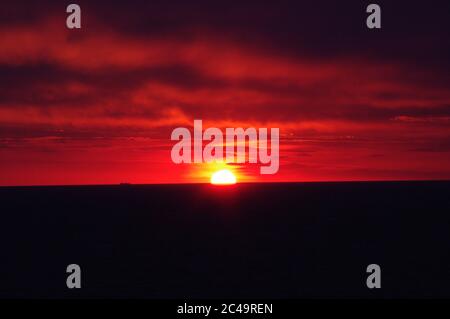 Séquence d'images d'un coucher de soleil, coucher de soleil rouge vif sur mer sombre avec nuages sombres Banque D'Images