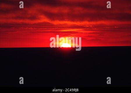 Séquence d'images d'un coucher de soleil, coucher de soleil rouge vif sur mer sombre avec nuages sombres Banque D'Images