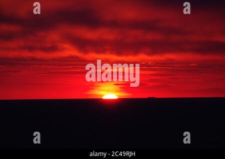 Séquence d'images d'un coucher de soleil, coucher de soleil rouge vif sur mer sombre avec nuages sombres Banque D'Images