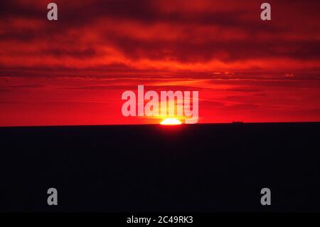 Séquence d'images d'un coucher de soleil, coucher de soleil rouge vif sur mer sombre avec nuages sombres Banque D'Images