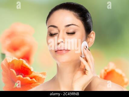 Belle femme brune avec tampon de coton sur fond fleuri. Concept de soins de beauté. Banque D'Images