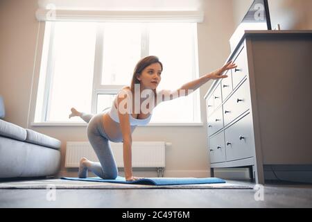 Femme enceinte qui se balance sur un genou et main sur le tapis de yoga Banque D'Images