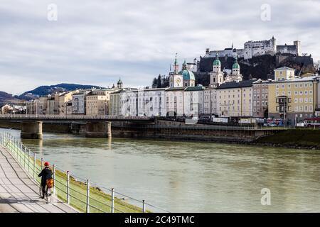 Salzbourg, Autriche - 5 mars 2017 : vue sur un cycliste qui fait du vélo le long de la rivière Salzach et de la vieille ville de Salzbourg en arrière-plan Banque D'Images