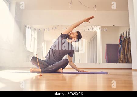 Beau jeune homme faisant de l'exercice d'étirement dans le studio de yoga Banque D'Images