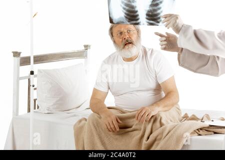 Vieux homme âgé se rétablissant dans un lit d'hôpital isolé sur fond blanc. Se soucier. Concept de soins de santé et de médecine. Médecin montrant des examens pulmonaires, rayons X pour les résultats du traitement. CopySpace. Banque D'Images