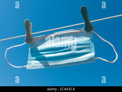 Masque jetable PPE, suspendu sur une ligne de lavage contre un ciel bleu Banque D'Images