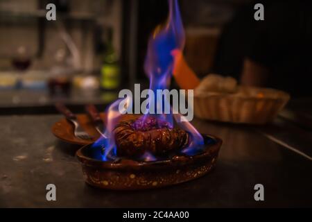 Saucisse traditionnelle portugaise churico aka chorizo espagnol tranché et cuit à la flamme sur l'alcool dans un plat en faïence à la table servi avec du pain Banque D'Images