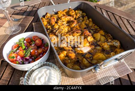 Poulet Aloo Gobi curry servi dans un plat à rôtir avec un moule à rôtir pour un dîner en plein air avec chutney à la tomate et à la menthe et yaourt au soleil, Royaume-Uni Banque D'Images