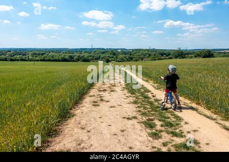 Un jeune garçon fait son vélo le long d'une piste de terre à travers un champ d'orge. Banque D'Images