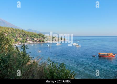 Lagon calme avec bateau à voile et bâtiments en forêt sur le flanc d'une colline. Bateau safari de plongée ancré dans la baie de Jemeluk Banque D'Images