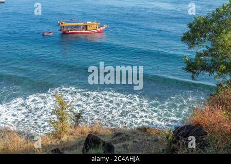 Lagon calme avec bateau à voile et bâtiments en forêt sur le flanc d'une colline. Bateau safari de plongée ancré dans la baie de Jemeluk Banque D'Images