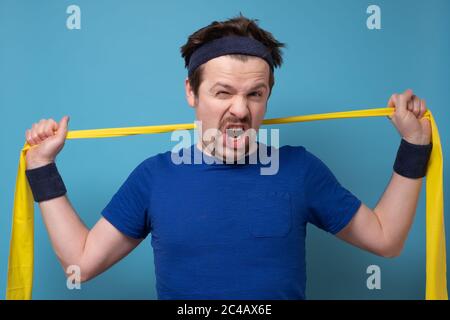 homme sportif s'exerçant avec un élastique sur un mur bleu. Banque D'Images