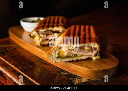 Sandwich traditionnel cubain au fromage, au jambon et au porc frit, servi sur un panneau de bois Banque D'Images