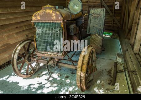 Un ancien tracteur de 100 ans avec démarrage à manivelle s'émiettant et rouillé dans un hangar obsolète d'équipement agricole Banque D'Images