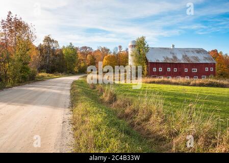 Grange traditionnelle rouge avec silo le long d'une route non pavée dans la campagne du Vermont au coucher du soleil Banque D'Images