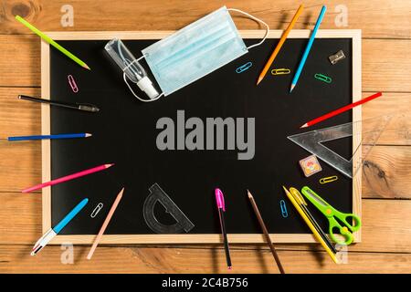 Divers fournitures scolaires, masque facial et gel hydroalcoolique sur tableau noir. Retour à l'école concept après la pandémie de covid19. Banque D'Images