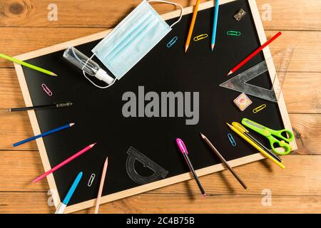 Divers fournitures scolaires, masque facial et gel hydroalcoolique sur tableau noir. Retour à l'école concept après la pandémie de covid19. Banque D'Images