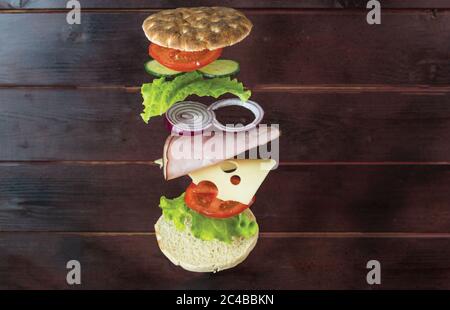 Vue rapprochée d'un sandwich maison avec des ingrédients volants sur fond de bois. Banque D'Images